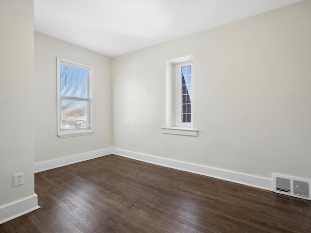 empty room with dark wood-style flooring, visible vents, and baseboards