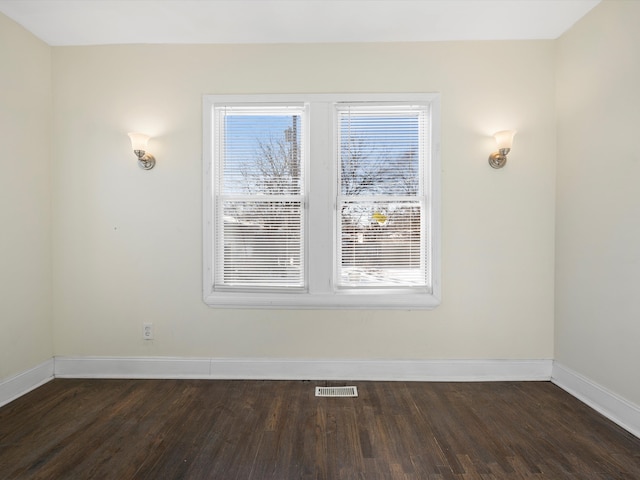 spare room featuring dark wood-style floors, visible vents, and baseboards