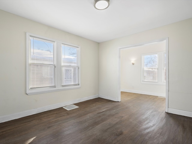 unfurnished room with dark wood-style floors, visible vents, and baseboards