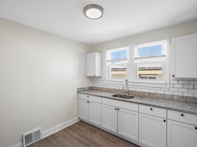 kitchen with dark wood-style flooring, tasteful backsplash, visible vents, white cabinets, and a sink