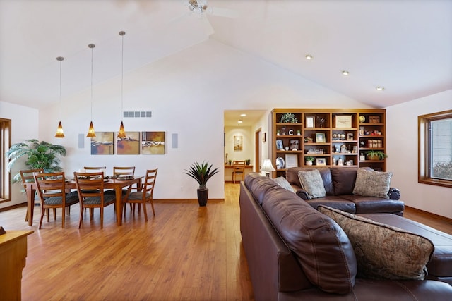 living room featuring visible vents, light wood-style flooring, ceiling fan, high vaulted ceiling, and baseboards