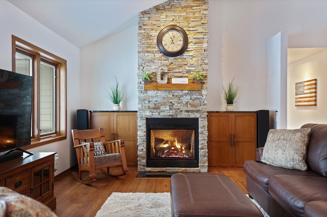 living room featuring light wood-style floors, lofted ceiling, and a stone fireplace