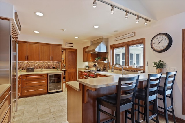 kitchen with wine cooler, a breakfast bar area, light countertops, a peninsula, and exhaust hood