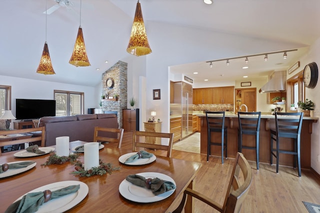 dining room with light wood-type flooring, recessed lighting, high vaulted ceiling, and a stone fireplace