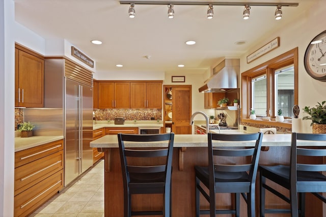 kitchen with light countertops, ventilation hood, built in refrigerator, and backsplash