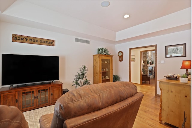 living room with light wood-type flooring, visible vents, a raised ceiling, and recessed lighting