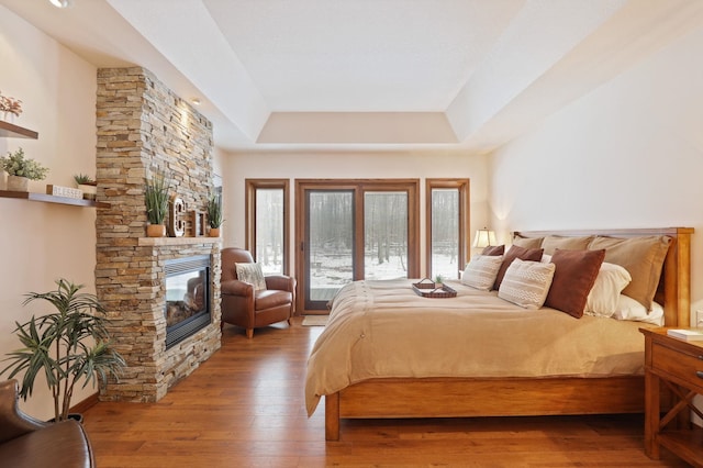 bedroom with access to outside, a fireplace, a raised ceiling, and wood finished floors