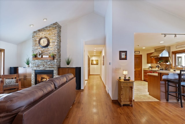 living area featuring high vaulted ceiling, light wood-type flooring, a fireplace, and baseboards