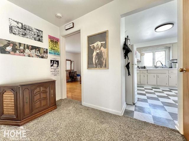 corridor with light floors, a sink, light colored carpet, and baseboards