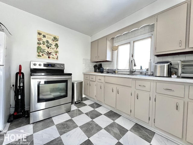 kitchen with tasteful backsplash, stainless steel electric range oven, light countertops, and a sink