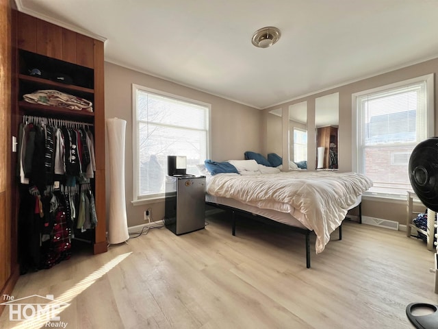 bedroom with light wood-style flooring, baseboards, a closet, and ornamental molding