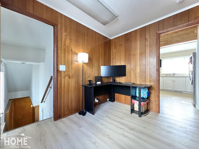 office area with a sink, wood walls, light wood-style flooring, and crown molding