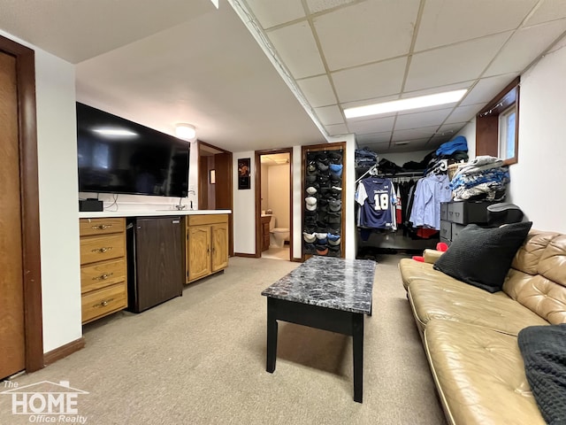 living area featuring light carpet, baseboards, and a drop ceiling