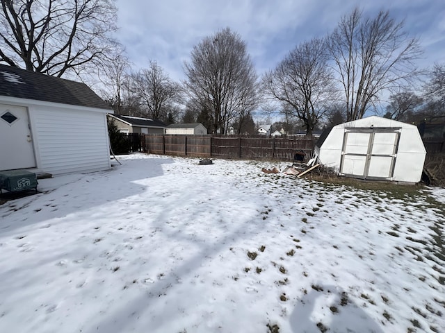 yard layered in snow with an outbuilding, a fenced backyard, and a shed