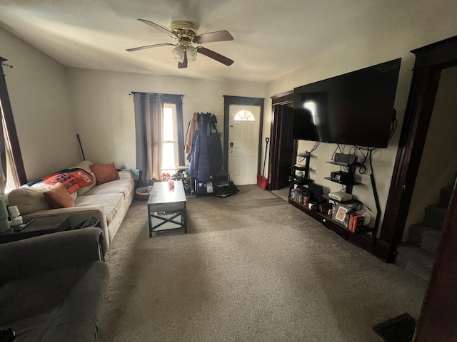 carpeted living room featuring a ceiling fan and stairway