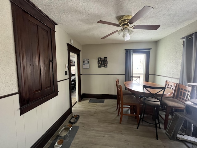 dining space with ceiling fan, a textured ceiling, dark wood-type flooring, and wainscoting