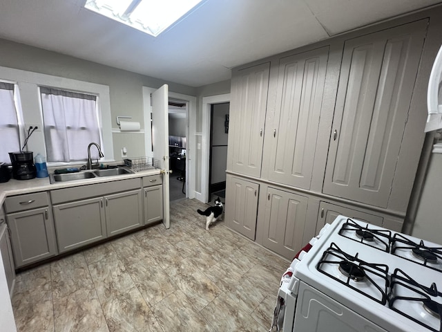 kitchen with gray cabinets, light countertops, a sink, and white gas range