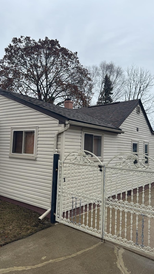 view of home's exterior with a shingled roof, a gate, and a chimney