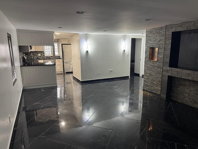 interior space featuring baseboards, marble finish floor, backsplash, stainless steel refrigerator, and dark countertops