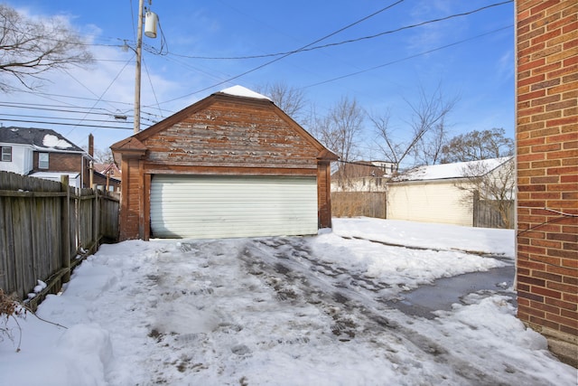 snow covered garage with a garage and fence