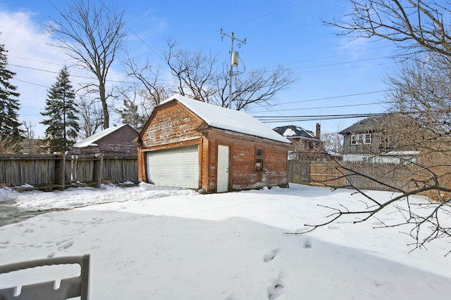 view of snow covered exterior with a detached garage, fence, and an outbuilding