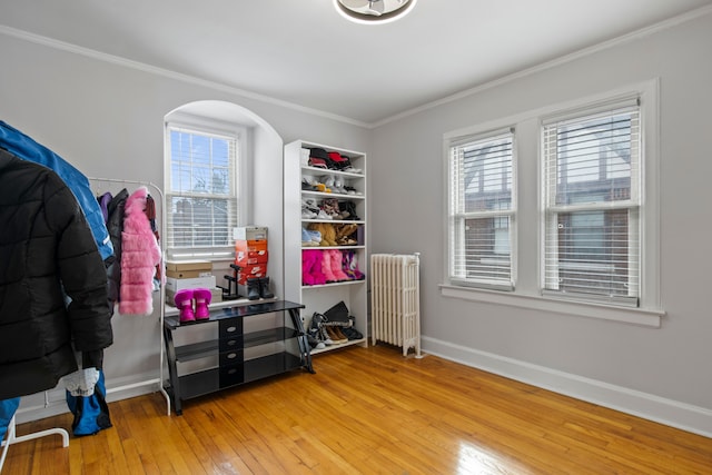 misc room featuring arched walkways, crown molding, light wood-style flooring, radiator heating unit, and baseboards