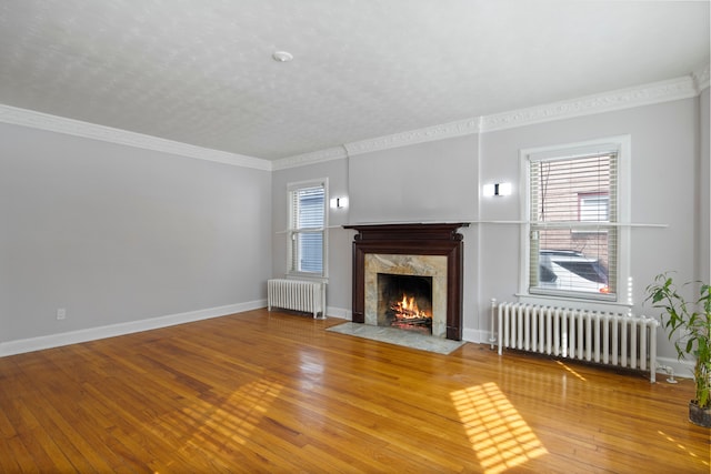 unfurnished living room with ornamental molding, a high end fireplace, radiator heating unit, and wood finished floors