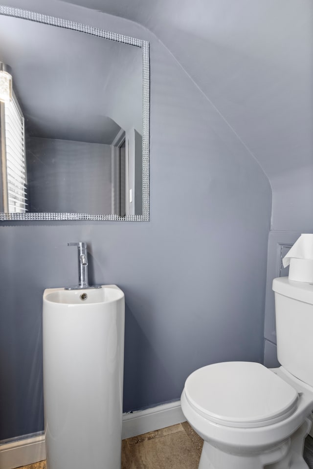 half bath with lofted ceiling, toilet, and baseboards