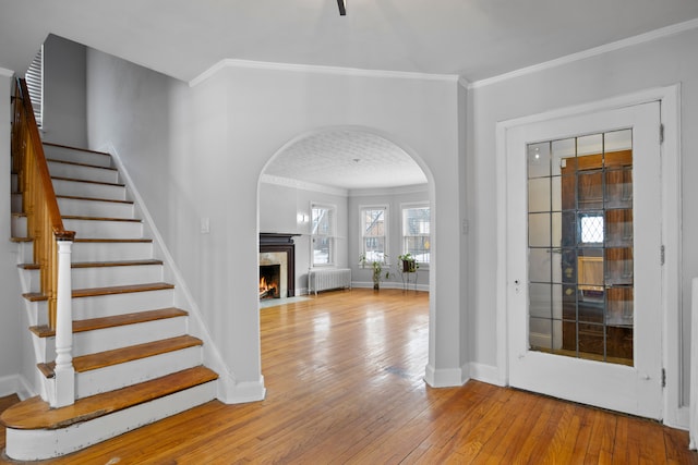 foyer entrance featuring arched walkways, crown molding, radiator, light wood-style flooring, and a premium fireplace