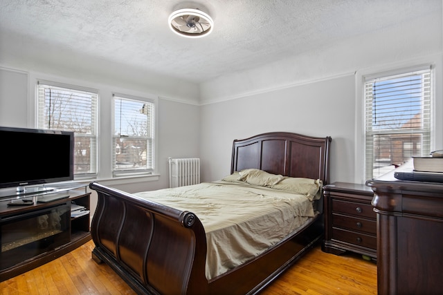 bedroom with light wood-style floors, radiator heating unit, and a textured ceiling