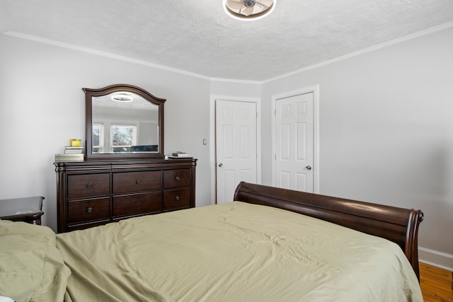 bedroom featuring a textured ceiling, ornamental molding, wood finished floors, and baseboards