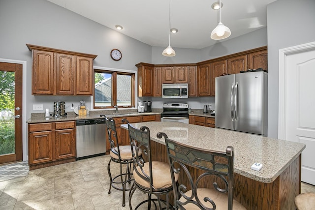 kitchen with decorative light fixtures, appliances with stainless steel finishes, a kitchen island, light stone countertops, and a kitchen bar