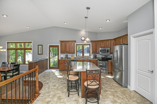 kitchen with stainless steel appliances, a kitchen island, a kitchen breakfast bar, hanging light fixtures, and light stone countertops