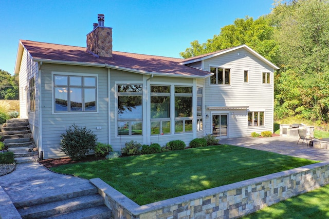 rear view of property with a chimney, a lawn, and a patio