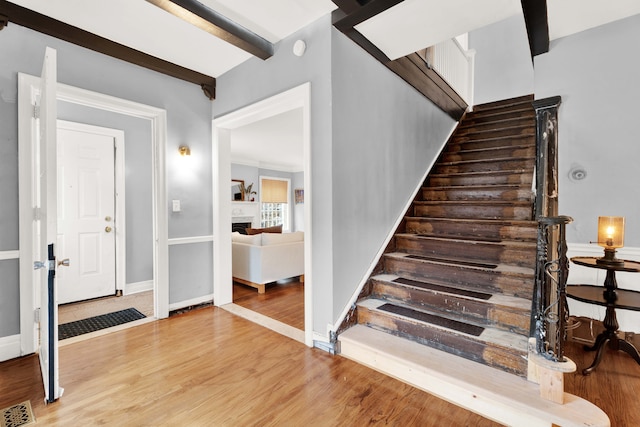 stairs featuring visible vents, baseboards, wood finished floors, beamed ceiling, and a fireplace