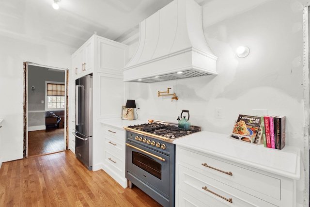 kitchen with premium appliances, light wood-style flooring, white cabinetry, light countertops, and custom range hood