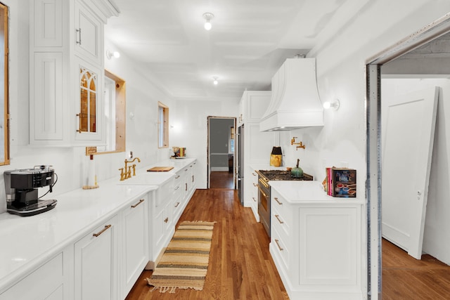 kitchen featuring white cabinetry, light countertops, custom exhaust hood, dark wood finished floors, and glass insert cabinets