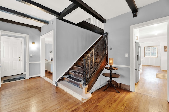 staircase with wood finished floors, beam ceiling, and baseboards