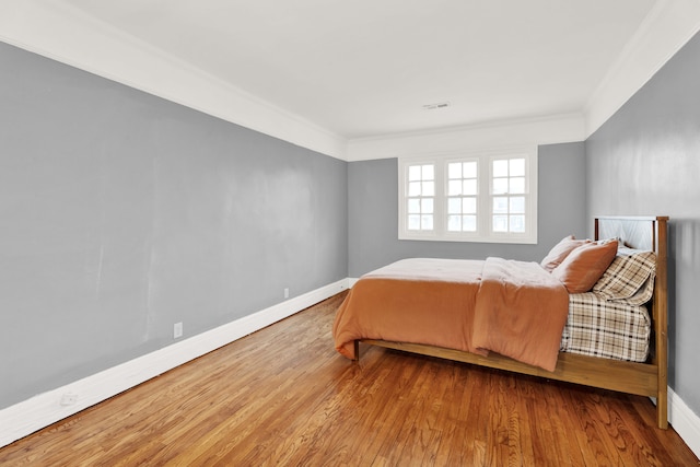 bedroom featuring ornamental molding, wood finished floors, visible vents, and baseboards