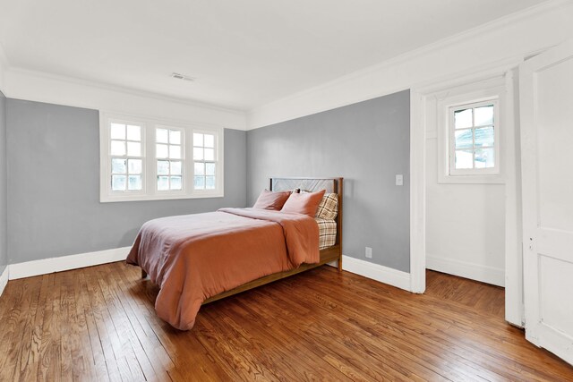 bedroom featuring visible vents, crown molding, baseboards, and wood finished floors