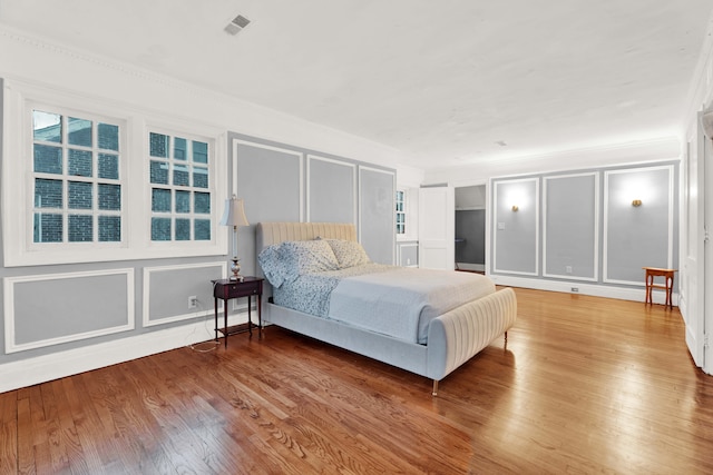 bedroom with ornamental molding, visible vents, a decorative wall, and wood finished floors