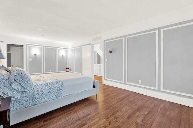 bedroom with visible vents, a decorative wall, and wood finished floors