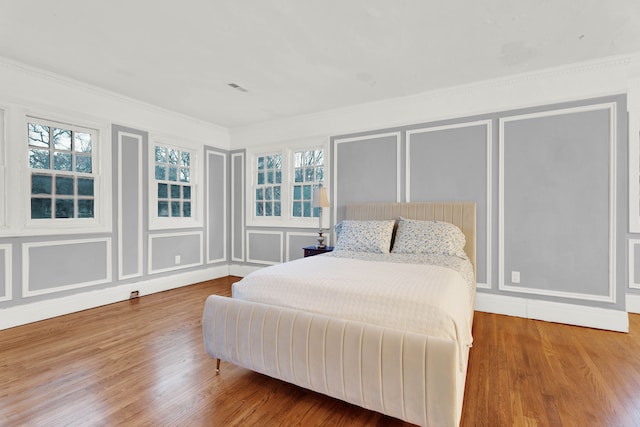 bedroom with ornamental molding, multiple windows, a decorative wall, and wood finished floors