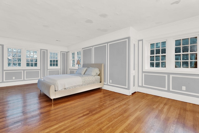 unfurnished bedroom with ornamental molding, a decorative wall, and wood finished floors