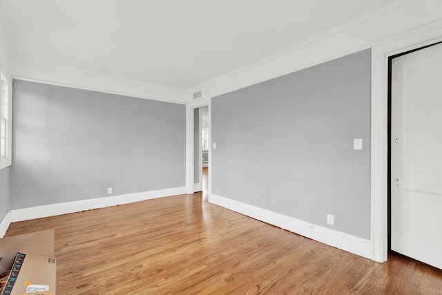 spare room with baseboards, wood finished floors, visible vents, and crown molding