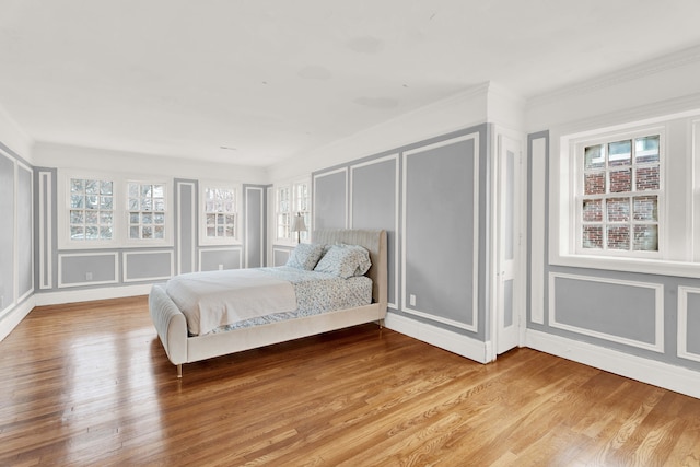 bedroom featuring multiple windows, a decorative wall, and wood finished floors