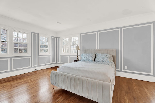 bedroom featuring visible vents, a decorative wall, and wood finished floors