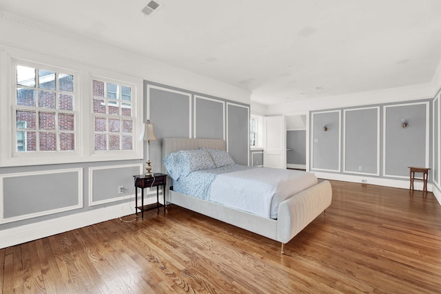 bedroom featuring wood finished floors, visible vents, and a decorative wall