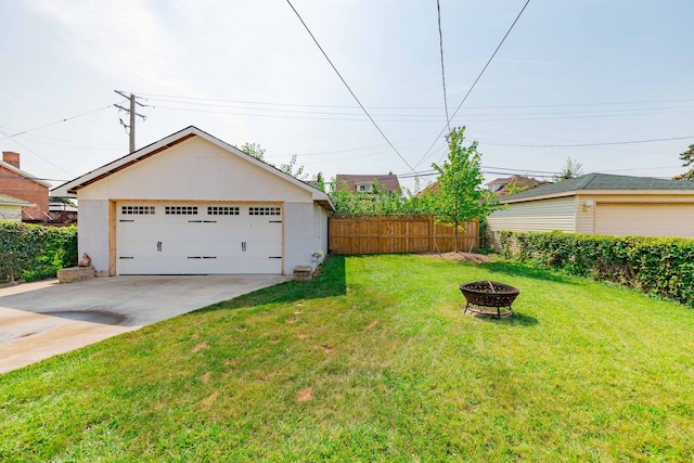 view of yard with a fire pit, a detached garage, fence, and an outdoor structure