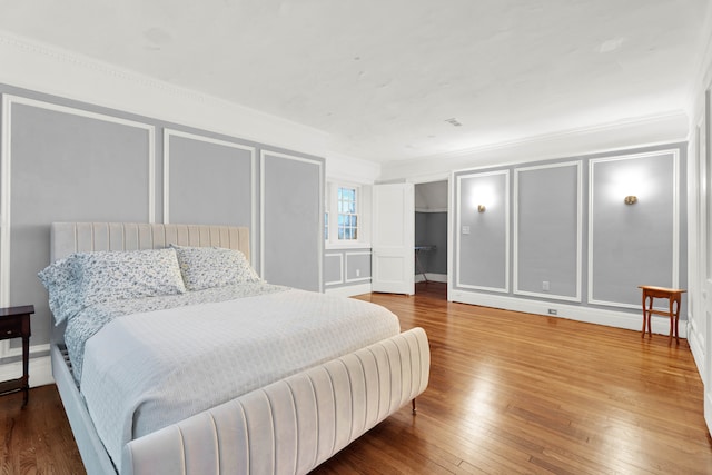 bedroom featuring a walk in closet, crown molding, a decorative wall, and wood finished floors